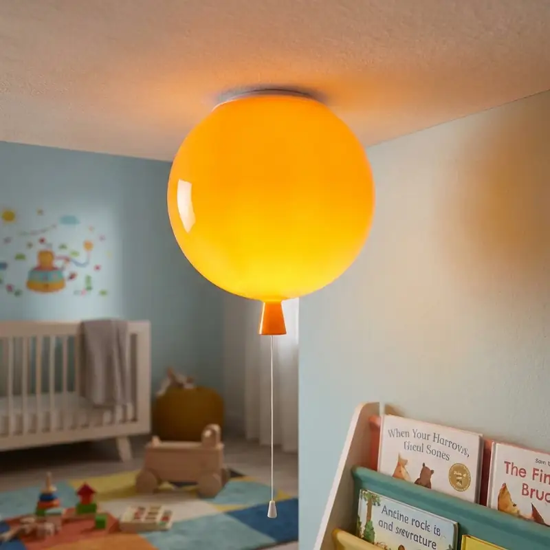 A whimsical yellow balloon-shaped ceiling light with a white pull cord switch, illuminated in a cozy modern nursery featuring a wooden crib and children's books.