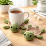 Handmade knitted turtle coasters on a wooden table, with a white coffee cup resting on one coaster, showing cute 3D animal design and cozy home use scene.