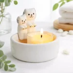 Minimalist ceramic cat candle holder with two cute cat figurines behind a glowing tealight, styled on a clean white surface with soft greenery for a cozy home decor scene.