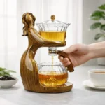 Creative gravity tea maker with artistic wooden sculpture, transparent glass teapots and flowing amber tea in a minimalist home tea scene.