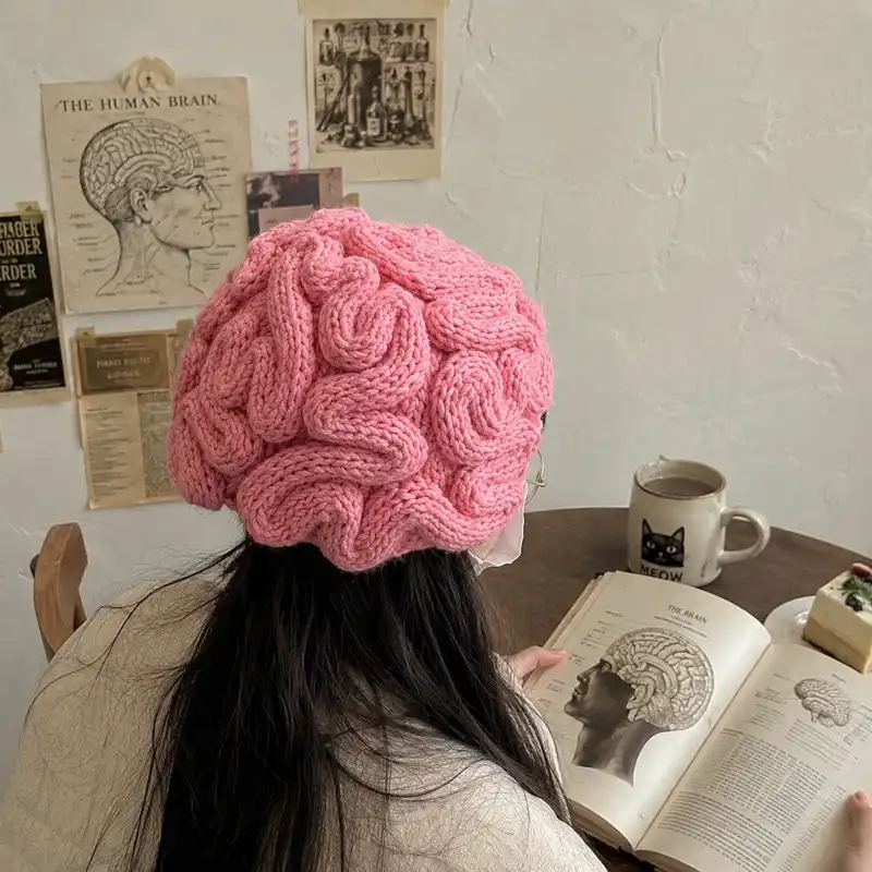 Person wearing a pink brain beanie with realistic knitted brain folds, photographed from behind in a casual indoor setting.