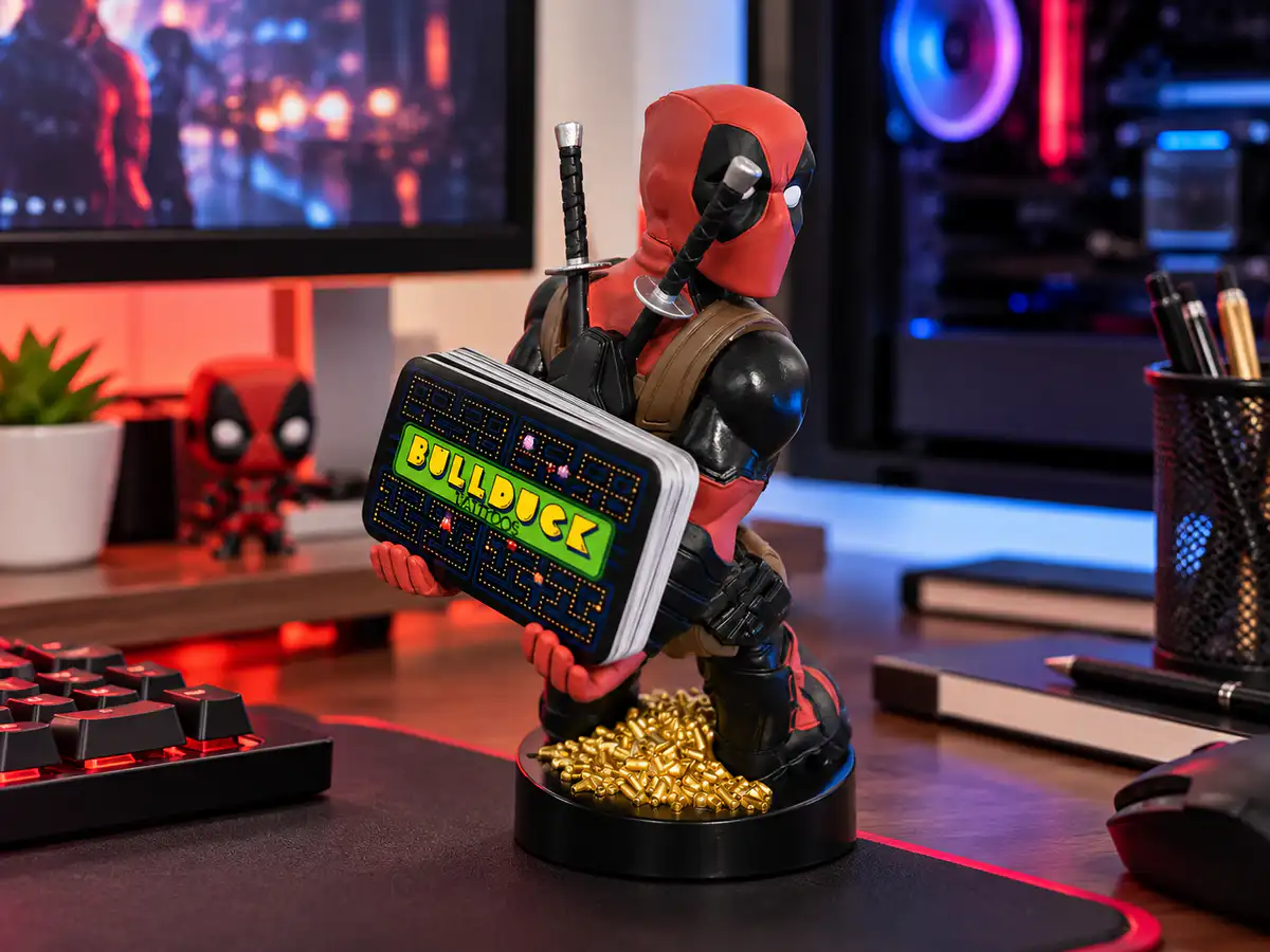 Deadpool Cable Guy figure in a red and black suit holding a stack of cards on a gaming desk with colorful RGB lighting.